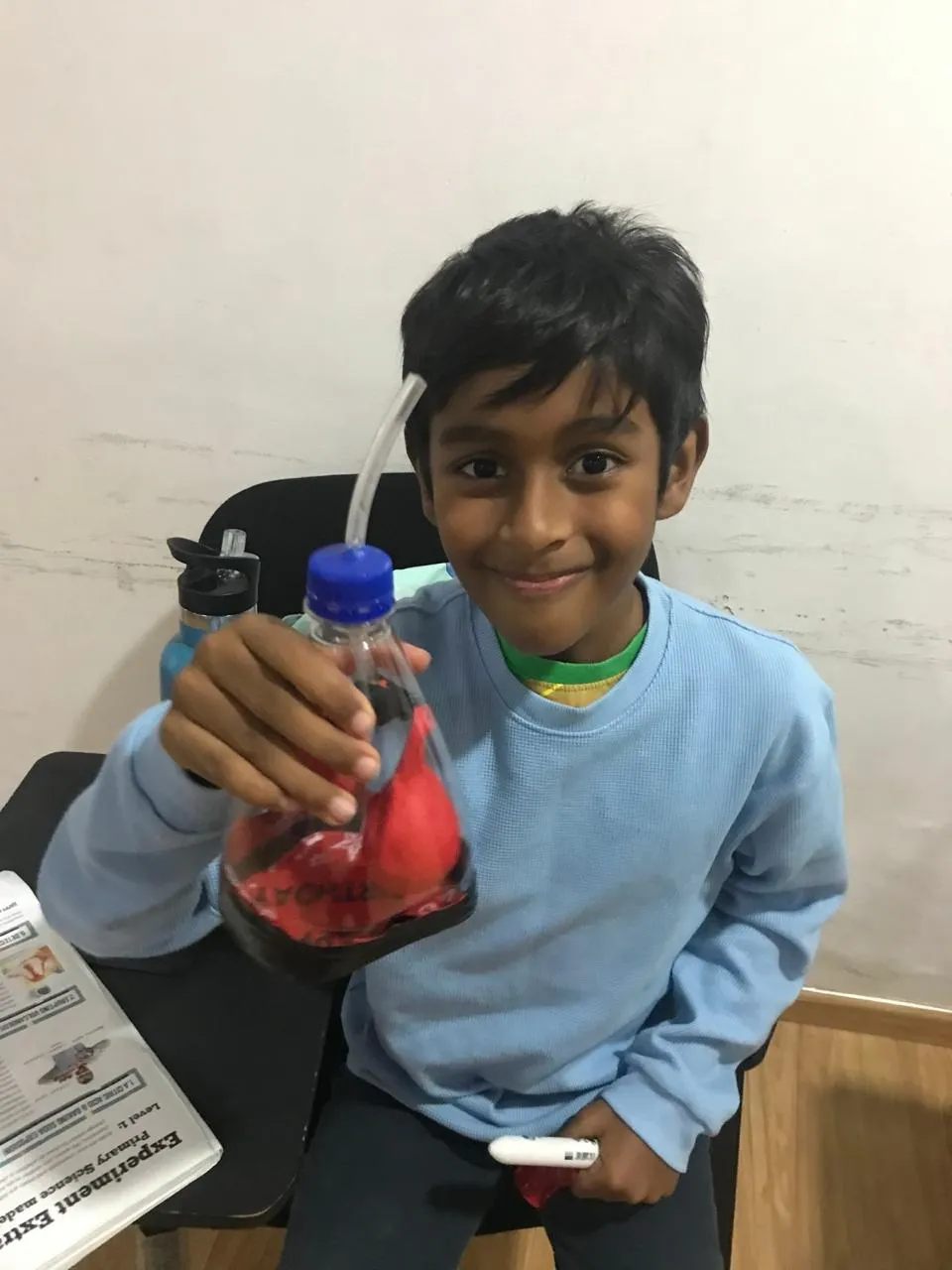 A smiling boy holding up a flask of deep red liquid he has just made