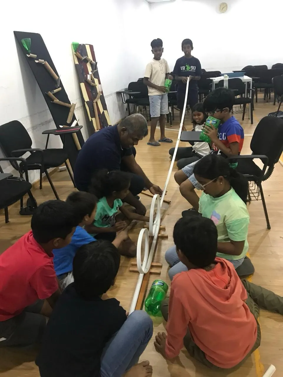 A large group of children building a marble run track on the floor with Mr. N