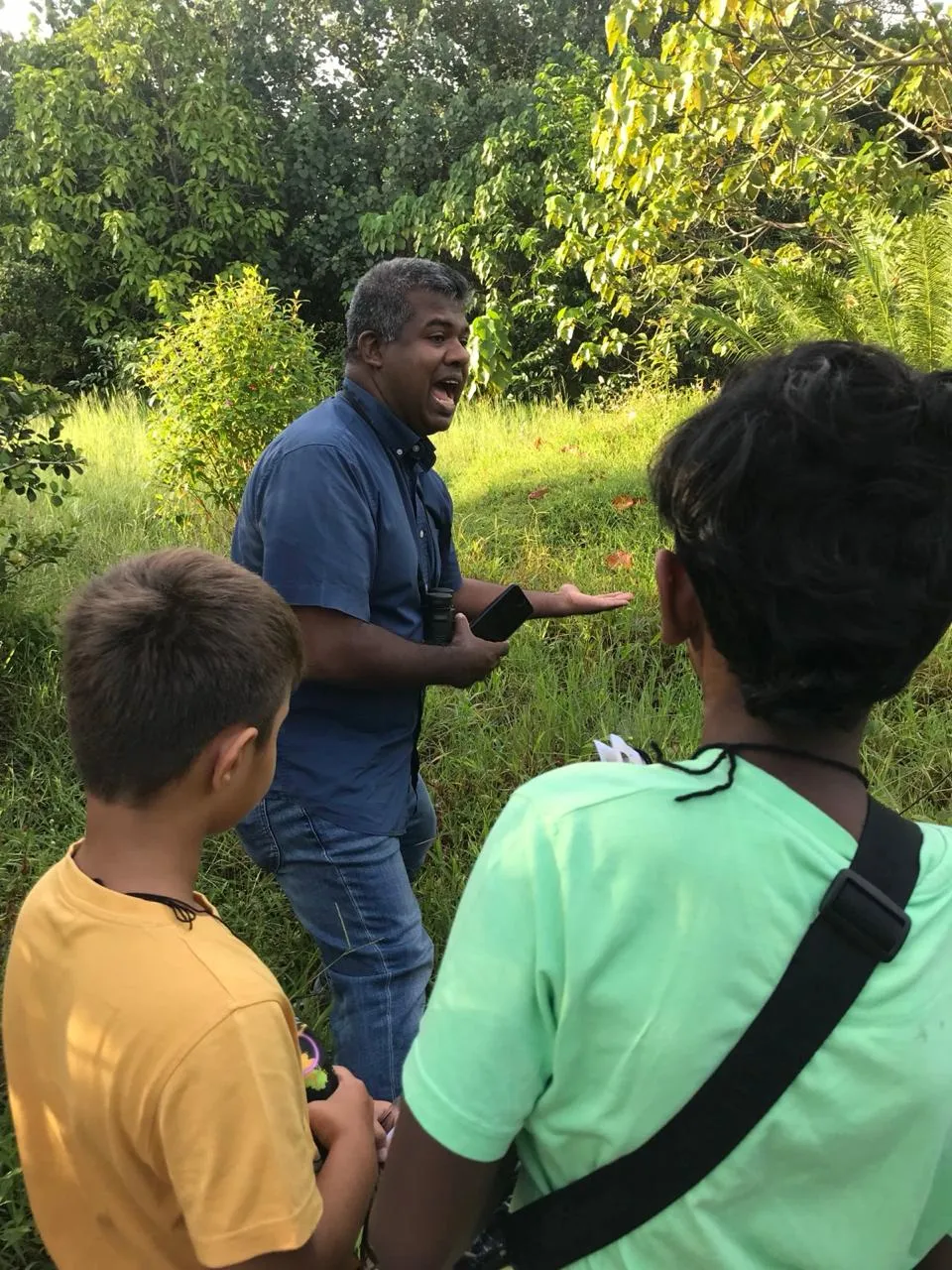 Mr. N talking to two children on a nature walk through long grass
