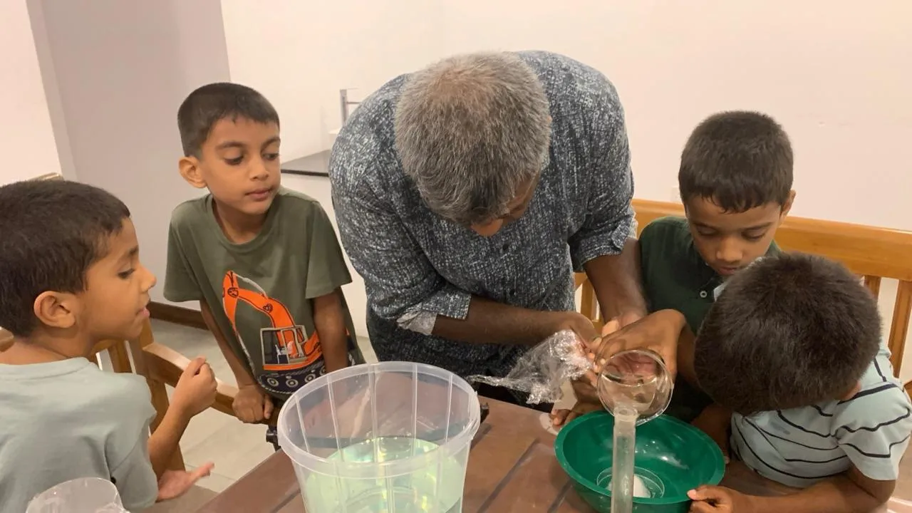 Mr. N pouring a reaction into a beaker while four children lean in to watch