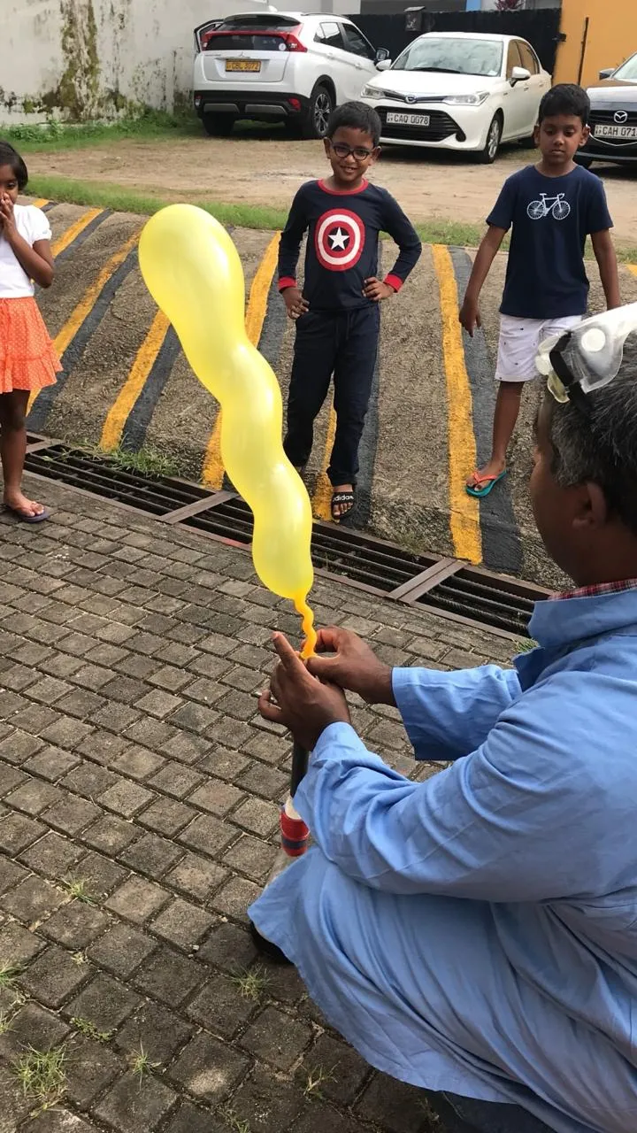 A long yellow balloon inflating from a flask while children watch from a distance